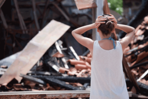 A woman is standing in front of a pile of rubble, contemplating why she didn't get earthquake insurance.